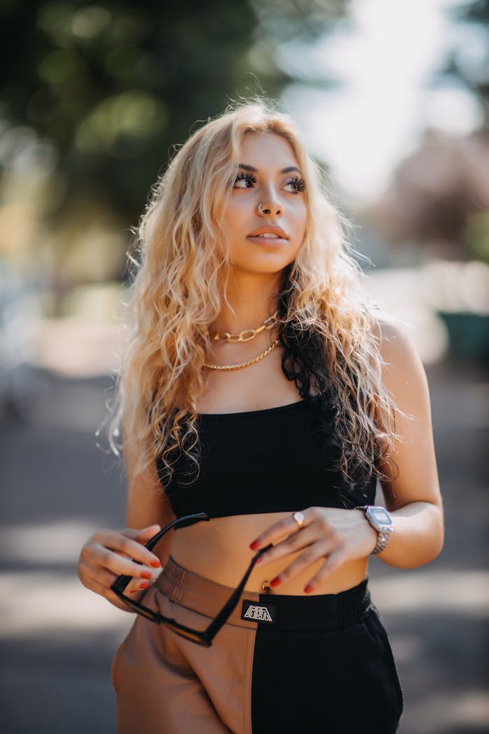 Blonde woman in casual fashion outdoors, wearing a black top and holding sunglasses.