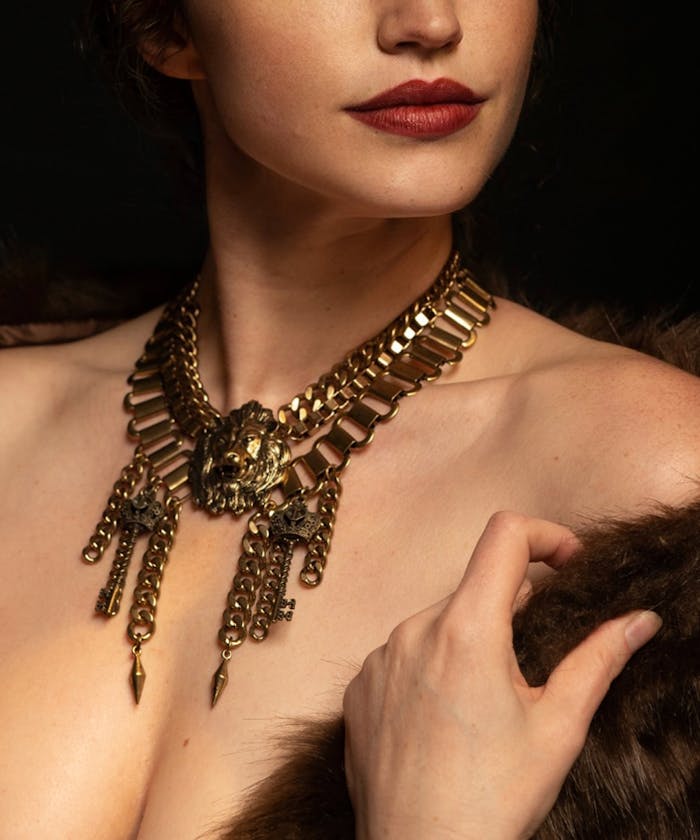 Close-up of a woman showcasing a luxurious gold statement necklace against a dark background.