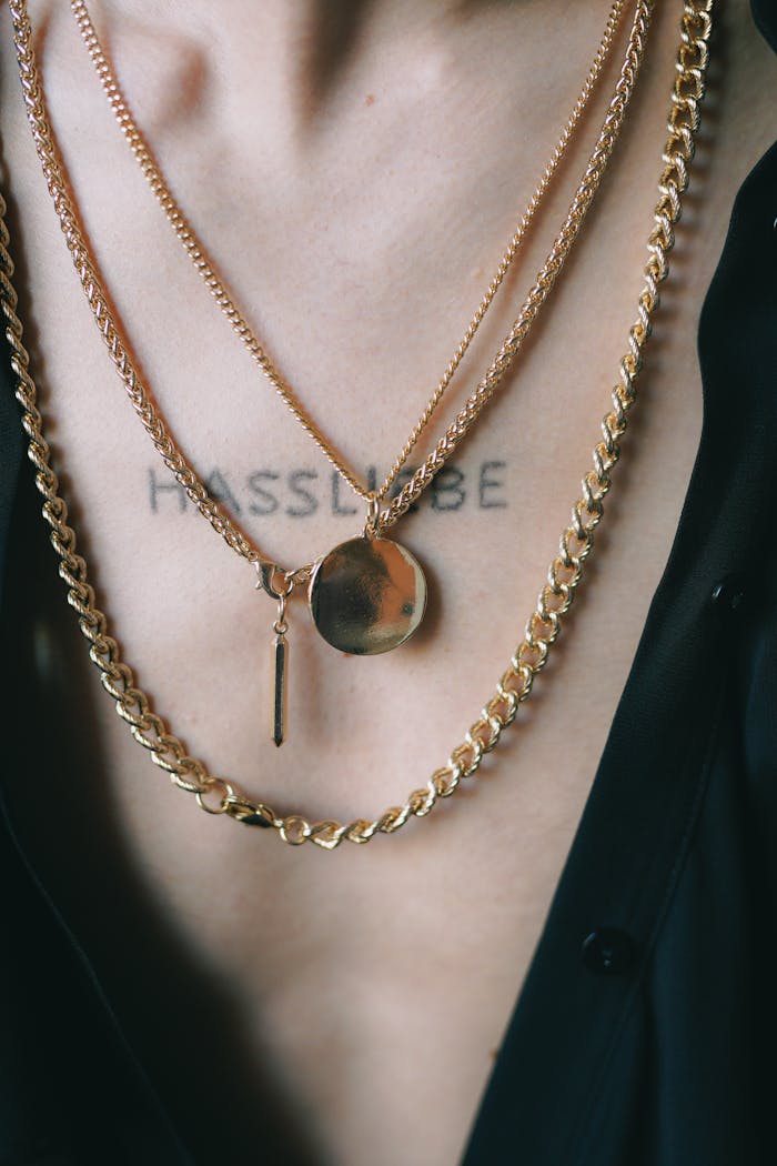 Detailed view of gold necklaces with a tattoo on a person's chest, showcasing fashion style.